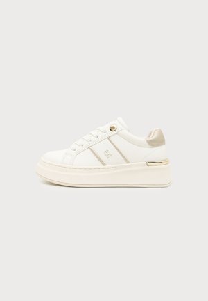 Hvid platformsneaker med snørebånd, metaløje, beige hæltab og præget logo på siden, vist i profil på ensfarvet baggrund.
