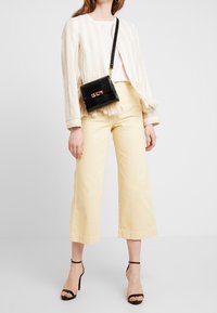 Blazer de rayas crema con flecos, top blanco, pantalones amarillos de pierna ancha, bolso negro con textura de cocodrilo y tacones negros con tira en el tobillo.