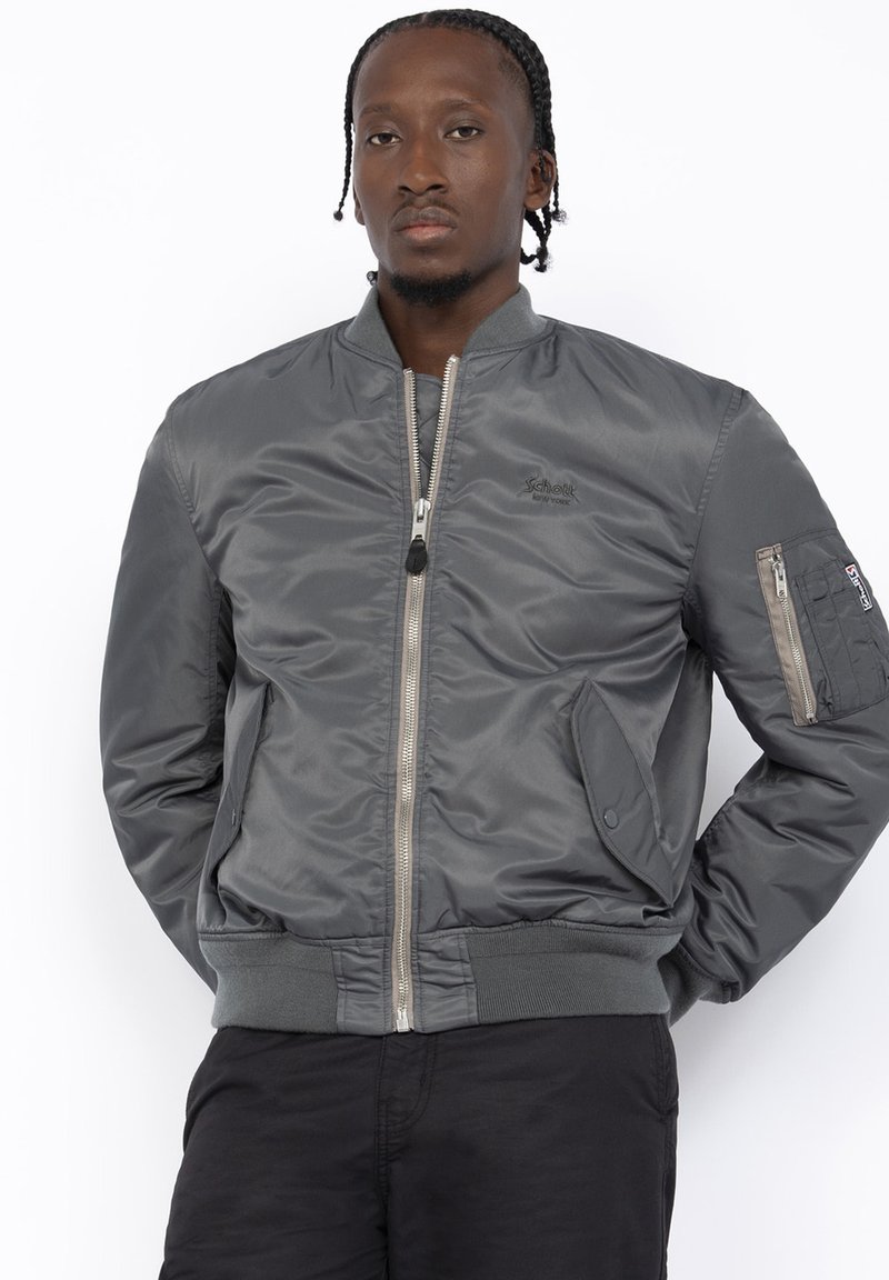 Giacca bomber grigia con chiusura zip, polsini e orlo a coste, due tasche laterali e una tasca aggiuntiva sul braccio. Texture liscia.