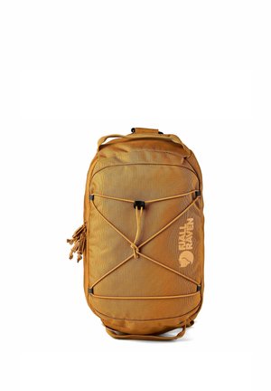 Mochila compacta marrón Fjällräven con cordón elástico delantero, bolsillos con cremallera y asa superior sobre fondo blanco.