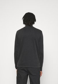 Schwarzes Langarm-Cotton-Sweatshirt mit Rundhalsausschnitt, Rückennähten und lässiger Passform, kombiniert mit passenden schwarzen Hosen.