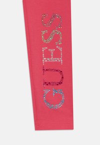 Rózsaszín leggings, melynek oldalán több színű strasszokkal a "SASS" felirat függőlegesen van elhelyezve. Sima tapintású, rugalmas anyag.