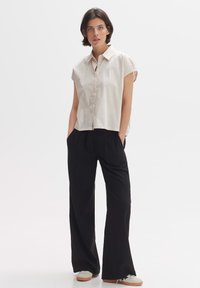 Light beige cropped blouse with a collar, short sleeves, and front buttons, paired with high-waisted black trousers and light sneakers.