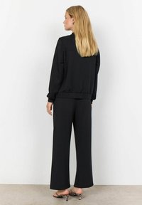 Svart tvådelad outfit bestående av en lös långärmad topp och vida byxor. Slät textur med elastiska ärmslut och midjeband.