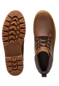 Bruine leren laarzen met een gladde afwerking, ronde neus en zwarte veters. Geprofileerde rubberen zool met een loopvlak voor grip. Clarks-logo aanwezig.