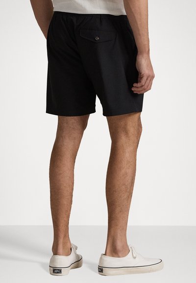 Black shorts with an elastic waist, featuring a back pocket and a button closure. Paired with white slip-on shoes.