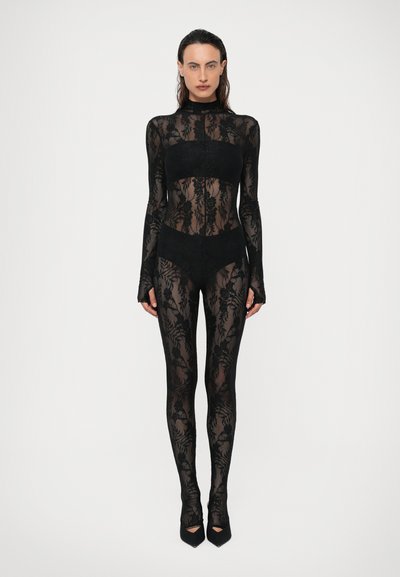 Body de encaje negro con mangas largas, cuello alto y patrones florales; diseño ajustado con tacones negros de punta abierta.