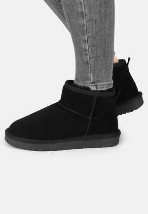Botas de tobillo de ante negro con una puntera suave y redondeada y un perfil bajo. Presentan un puño plegable y una suela de goma texturizada para mayor tracción.