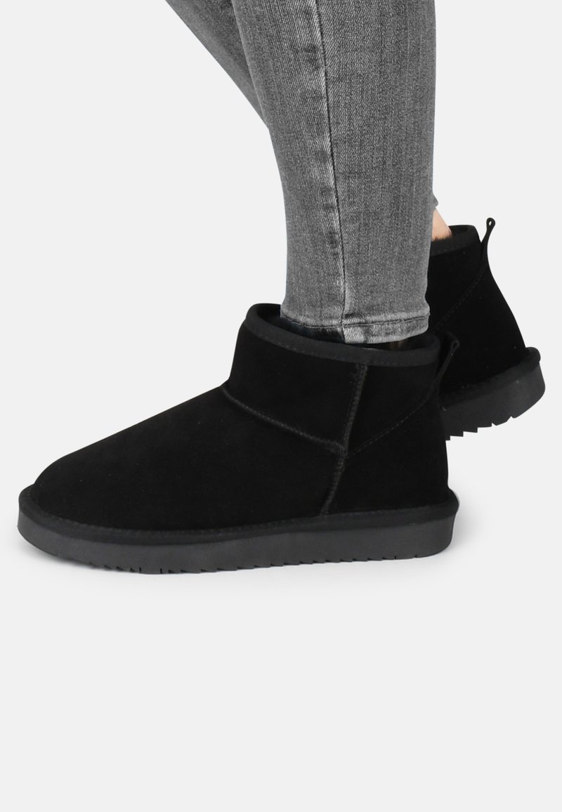 Botas de tobillo de ante negro con una puntera suave y redondeada y un perfil bajo. Presentan un puño plegable y una suela de goma texturizada para mayor tracción.