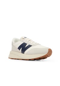 Sneaker de couleur crème avec des accents bleu marine et une semelle en caoutchouc. Comprend un dessus texturé, des lacets plats et un logo bien visible. Design à profil bas.