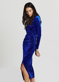 Vestito in velluto blu con maniche lunghe, design avvolgente e dettagli arricciati sul lato, con uno spacco alto sulla coscia all'orlo.