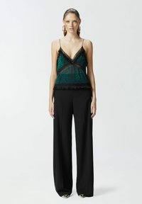 Prozirna zelena bluzica s uzorkom leoparda, čipkastim rubom i crnim akcentima, u kombinaciji s visokim crnim širokim hlačama.