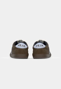 Baskets en suede marron avec un empiècement en cuir blanc au talon et une marque "VEJA". Forme arrondie avec une semelle en caoutchouc texturée et un design minimaliste.