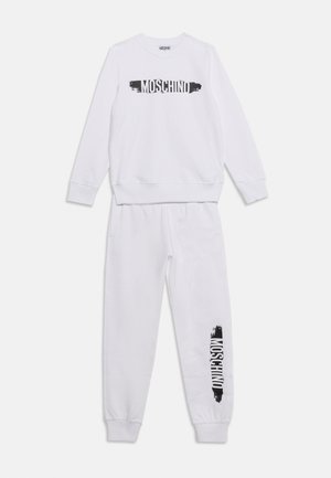 Biely set Moschino s mikinou a teplákmi s čiernym logom na prsiach a ľavej nohe, zobrazený naplocho na bielom pozadí.