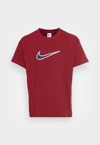 Červené bavlněné tričko s bílým a námořnickým logem Nike swoosh na přední straně. Krátké rukávy a kulatý výstřih. Hladká texturka.