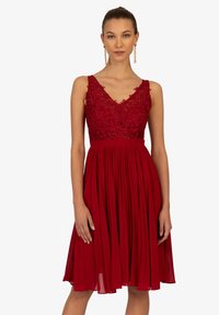 Abito rosso aline con bodice in pizzo, scollatura a V e gonna plissé. Presenta spalline regolabili e un tessuto leggero e fluido.