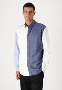 Chemise boutonnée avec un design en color-block : bleu marine, bleu clair et blanc. Présente une poche sur la poitrine et une coupe décontractée. Tissu de coton lisse.