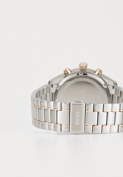 Montre en acier inoxydable avec un bracelet en argent poli et des accents dorés. Caractéristiques d'un cadran rond, de trois boutons-poussoirs et du logo de la marque.