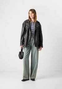Svart skinnbikerjakke over en grå rutete bluse, ved siden av vide lys blå jeans og svarte ankelstøvler. Svart flettet håndveske.