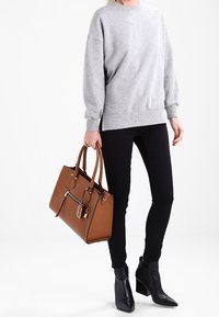 Szara bluza o luźnym kroju, czarne rurki oraz brązowa torba na ramię z uchwytami i suwakiem. Czarne botki na obcasie dopełniają stylizację.