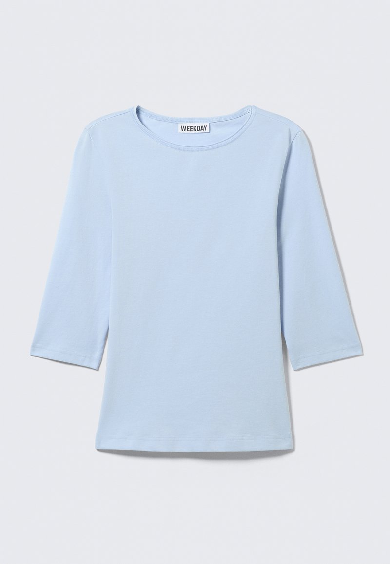 Chemise bleu clair à manches longues avec col rond, design uni, et étiquette "WEEKDAY" au dos du col.