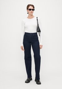 Tummansiniset korkeavyötäröiset farkut, puuvillasekoitetta, suorat lahkeet, yhdistetty valkoiseen pitkähihaiseen paitoihin ja mustiin asusteisiin. Sileä pinta, minimaalinen design.