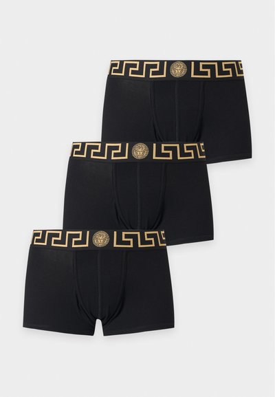 Trois boxers noirs avec un motif de clé grecque dorée et un logo tête de Méduse sur la ceinture, disposés en diagonale sur un fond blanc.