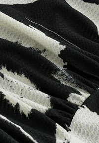 Texturovaná tkanina s černobílým abstraktním vzorem, s různými odstíny a vrstvením, které vytváří hloubku a vizuální zajímavost.