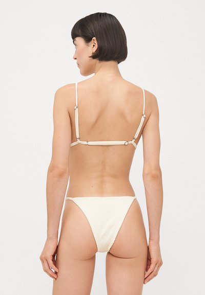 Crème-kleurige bikini set met gestructureerde stof, dunne bandjes en verstelbare hardware aan de achterkant. Minimalistisch ontwerp met een low-rise snit.