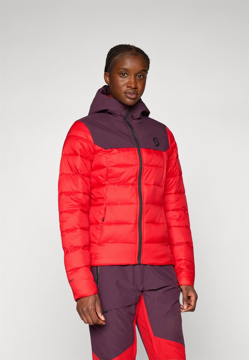 Czerwona i fioletowa kurtka puchowa z zamkiem błyskawicznym, kapturem i poziomymi wzorami pikowania; posiada logo na lewej stronie klatki piersiowej.