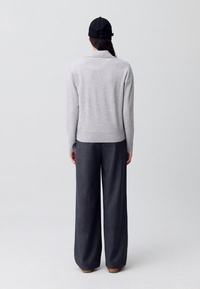Maglione grigio lavorato a maglia con colletto, abbinato a pantaloni larghi scuri. Il modello indossa un berretto nero, mostrando una vestibilità rilassata e una texture morbida.