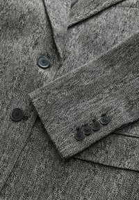 Blazer grigio a spina di pesce con rever, dotato di bottoni neri e tessuto testurizzato. Include quattro bottoni sul polsino della manica.