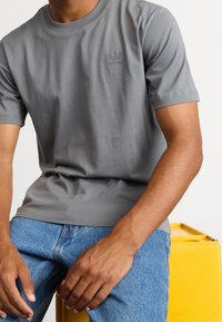 Gray short-sleeve T-shirt made of cotton with a round neckline and a small green logo on the chest. Paired with blue jeans.