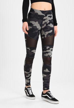 Leggings en camouflage noir et gris avec des panneaux en maille transparente et une taille élastique, conçues pour le confort et la flexibilité dans les vêtements de sport.