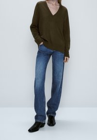 Olijfgroene v-hals trui, losse pasvorm, geribde manchetten en zoom, gecombineerd met lichtblauwe recht gesneden spijkerbroeken en zwarte enkellaarsjes.