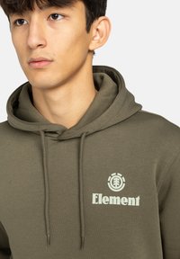 Felpa cappuccio verde oliva realizzata in morbido tessuto, con tasca a marsupio, presenta un logo circolare e il testo "Element" in colore chiaro sul petto.