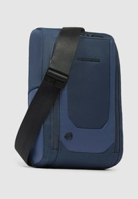 Bolsa de mensajero azul hecha de nylon texturizado, con un bolsillo frontal con cremallera, correa negra ajustable y detalle de logo en el lateral.