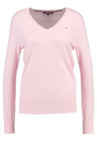 Jasnoróżowy sweter w serek z długimi rękawami, wykonany z miękkiego materiału dzianinowego, z małym logo na lewej stronie klatki piersiowej.