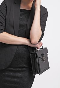 Černá kožená kabelka se strukturovaným designem, horní rukojetí a předním klopou s kovovým zapínáním. Hladká textura s jemnými detaily.