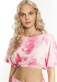 Top cropped rosa tie-dye con maniche a sbuffo corte e orlo elastico, realizzato in tessuto morbido e leggero. La modella ha i capelli lunghi e mossi.