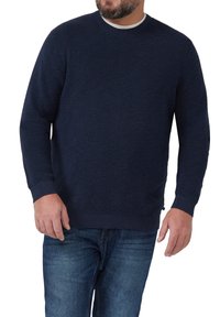Granatowy sweter z teksturowanym wzorem dzianiny, okrągłym dekoltem i ściągaczami przy rękawach. Noszony z niebieskimi dżinsami o luźnym kroju.