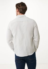 Camisa de manga larga a rayas azul claro y blanca, hecha de una tela suave, que presenta un canesú en la parte posterior y puños abotonados, combinada con jeans de mezclilla oscura.