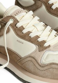 Beige und cremefarbene Sneaker aus Wildleder und synthetischen Materialien, mit strukturierten Mustern, dicken Schnürsenkeln und einem Logo an der Seite.