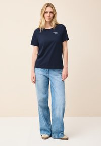 T-shirt en coton bleu marine à manches courtes, avec le logo "sempre" brodé en bleu clair sur la poitrine gauche, associé à un jean large bleu clair.