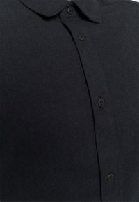 Zwart herringbone overhemd met een kraag, voorzien van een rij donkere knopen en een gestructureerde stof. Close-up van het materiaal en het ontwerp.