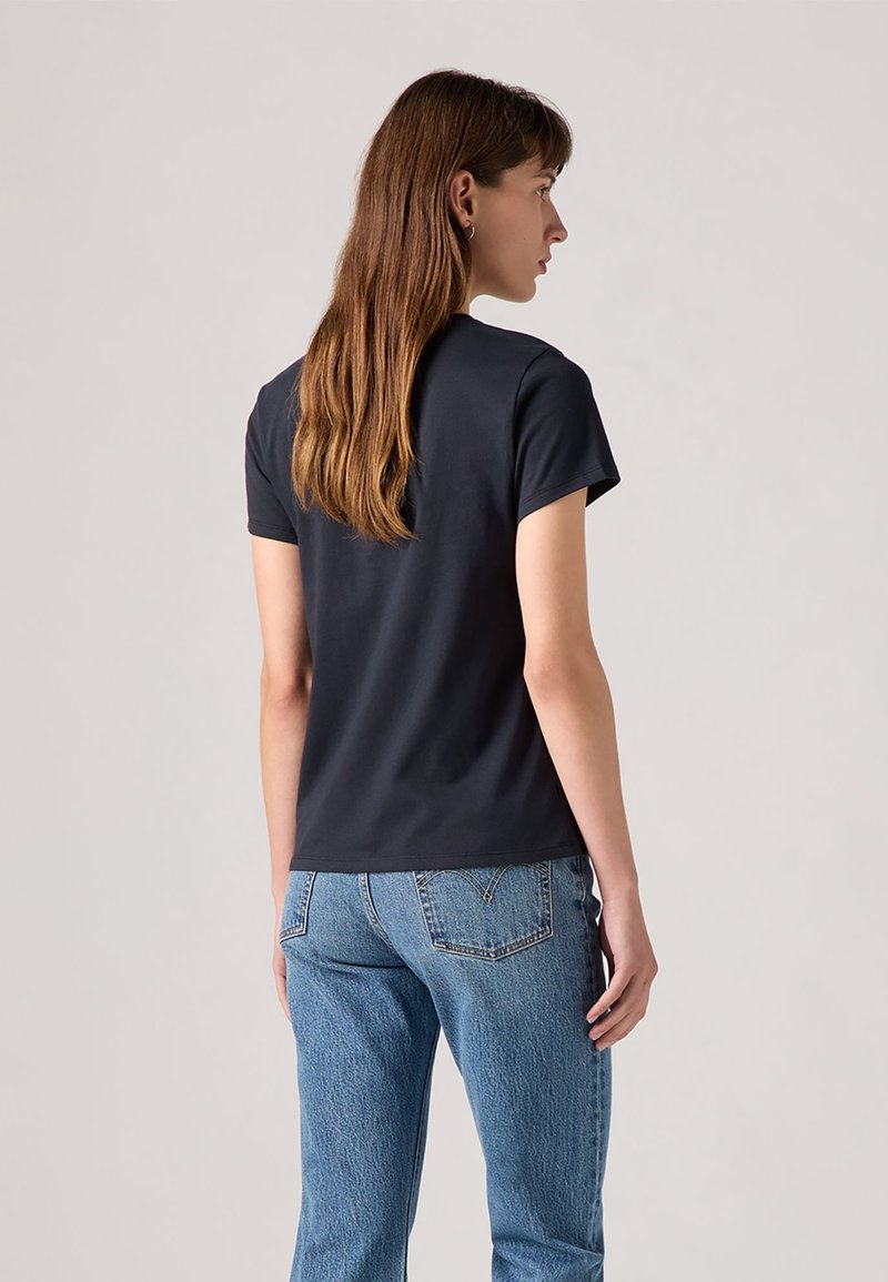 Schwarzes Kurzarm-T-Shirt mit tailliertem Design, kombiniert mit hellblauen, abgetragenen Jeans. Der Stoff wirkt glatt mit einem einfachen Halsausschnitt.