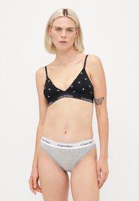Fekete háromszög melltartó fehér ismétlődő logó mintával, rugalmas pánttal, melyen a "Calvin Klein" felirat szerepel. Szürke, alacsony derekú bugyi fehér logós derékpánttal.