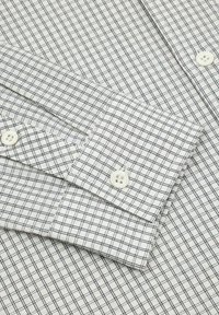 Biała koszula z drobnym czarnym wzorem kratki. Posiada mankiety zapinane na guziki oraz białe guziki. Gładka bawełniana tkanina o wyraźnym, świeżym wyglądzie.