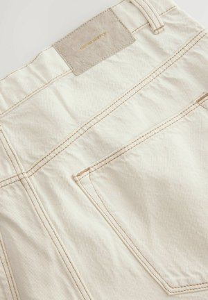 Beżowe bawełniane spodnie z cienkimi pionowymi paskami, z skórzaną naszywką oznaczoną "DENIM SUPPLY" i kontrastowym ściegem na kieszeniach.