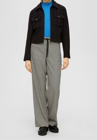 Zwarte cropped jas met twee voorzakken, gecombineerd met hooggesneden zwart-witte houndstooth patroonbroeken. Zwarte platform schoenen.